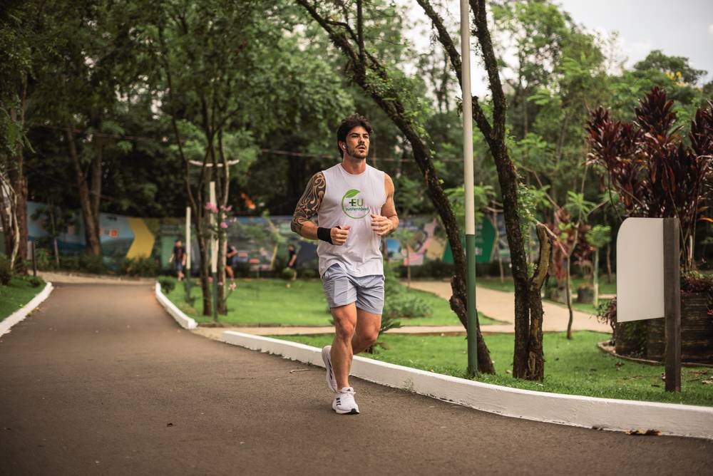 Thiago correndo em um parque arborizado, com a camiseta do Eu Mais Sustentável