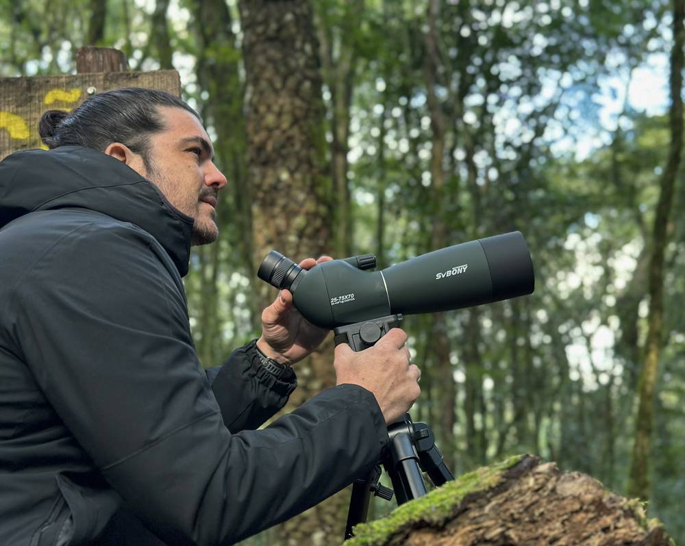 Thiago observando aves com uma luneta na mata da Flona